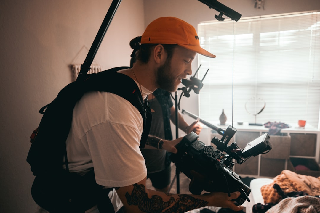 man in white shirt and orange cap holding black camera